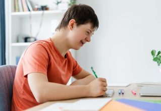 Boy Sits At A Desk, Focused On Writing In A Notebook With A Pencil In Hand — Gleam Support Services Pty Ltd in Weston, NSW