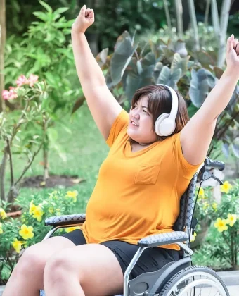 Woman In A Wheelchair Joyfully Raises Her Arms — Gleam Support Services Pty Ltd in Weston, NSW
